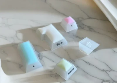 A set of TAPÉ Daydream pastel mechanical keyboard keycaps on a marble surface, ideal for comfortable typing with long nails.